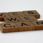 Scrabble tiles spelling 'Yes We Can' on a white background, conveying encouragement.